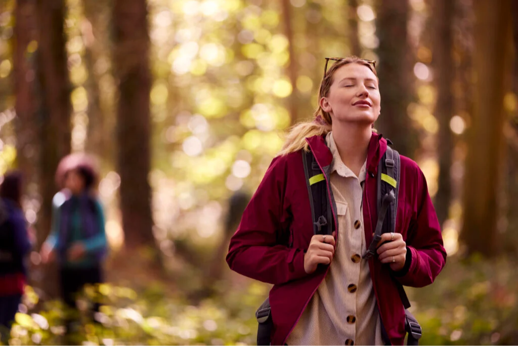 A hiker pauses with eyes closed in a sunlit forest