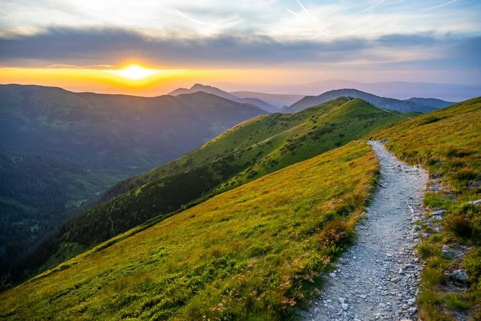 A person seated on a ridge at golden hour, looking out over the valley
